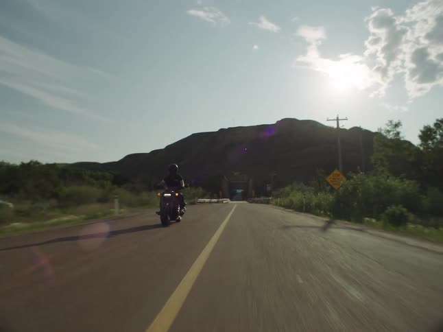 A man rides a motorcycle across a bridge in a remote area
