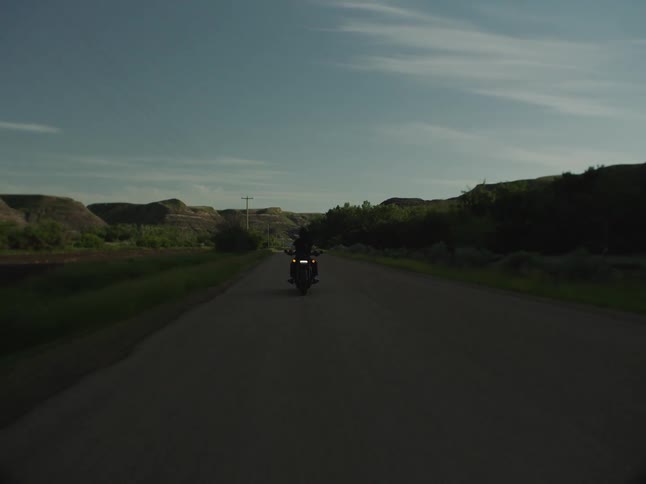 Motorcyclist rides along a highway through the rural countryside on a cloudy day near dusk