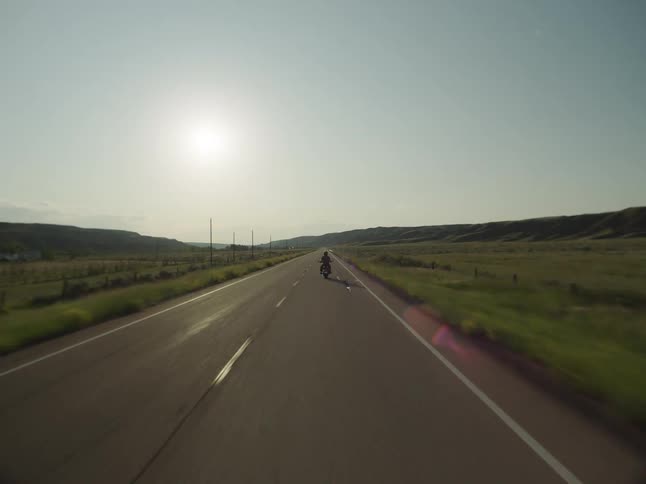 Motorcyclist rides along a road lit by the low sun on the horizon