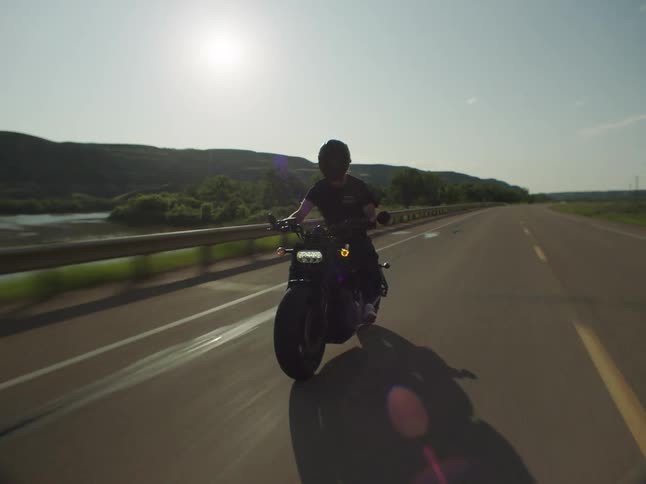 Motorcyclist speeds straight ahead under the clear sunny sky