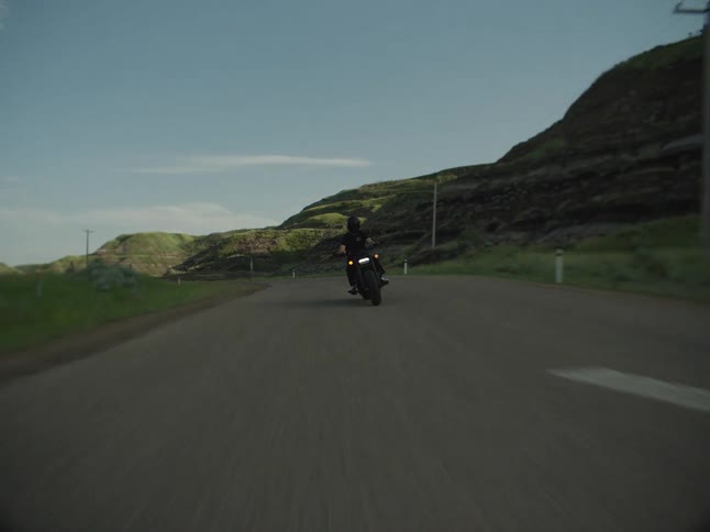 A person riding a motorcycle on a rural road passing fields hills mountains and utility poles