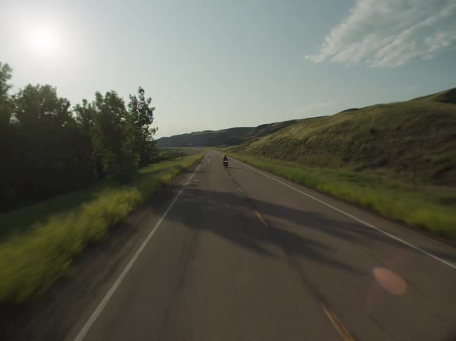 Motorcyclist rides along a road surrounded by hills under a clear sky