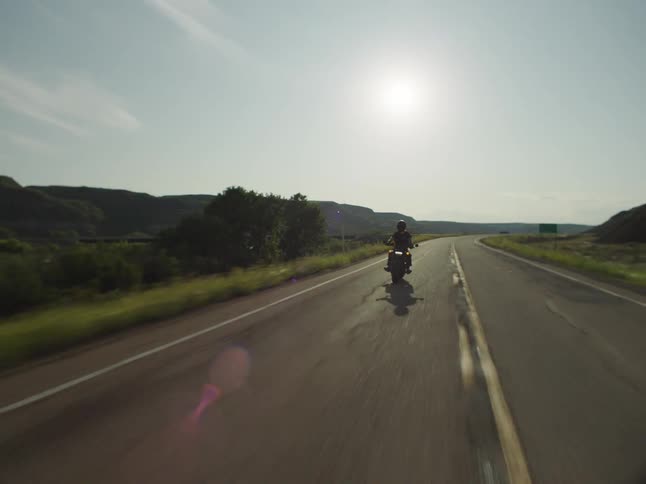 An adult rides a motorcycle on a rural highway on a sunny day