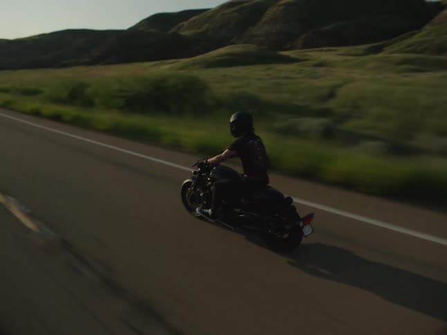 Motorcyclist rides along a road lit by the low sun amid the countryside