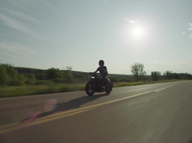 A person riding a motorcycle on a rural road passing utility poles next to the road and grass fields