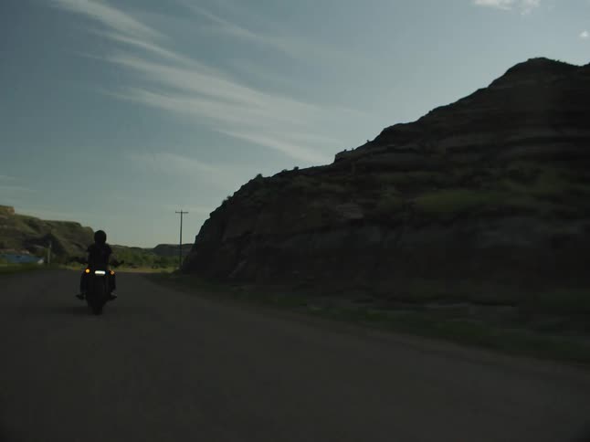 An adult rides a motorcycle on a remote road in a mountainous area