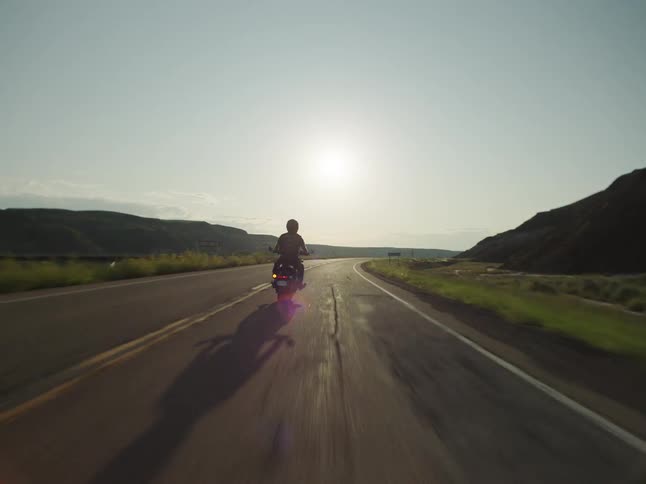 A person riding a motorcycle on a rural road headed towards the coast with the ocean on the horizon