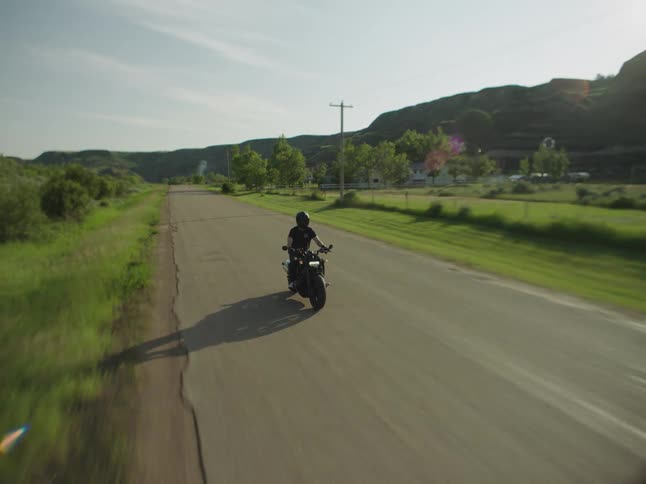 A person riding a motorcycle on a rural road passing utility poles by the road trees grass fields and hills