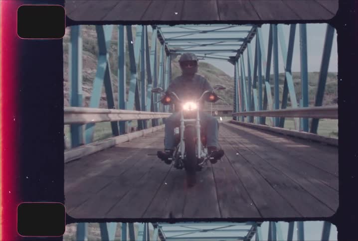 Motorcyclist crosses a wooden bridge surrounded by a blue metal structure