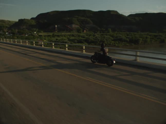 A person riding a motorcycle over a road bridge with a large river under it