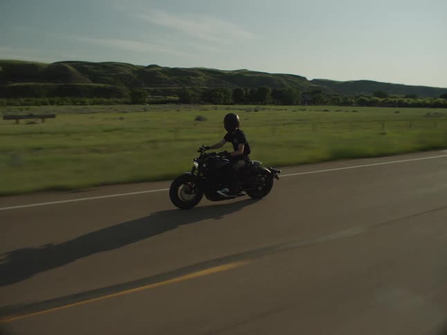 A person rides a motorcycle on a countryside highway at midday wearing a helmet