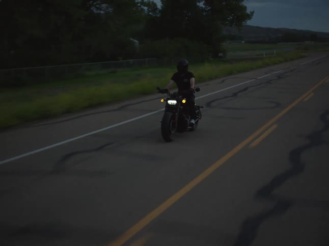 At dusk a motorcyclist travels down an empty twolane road headlight and amber signals glowing