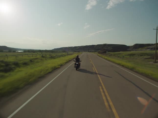 Male motorcyclist travels along a highway passing multiple hills in the rural countryside on a cloudy day
