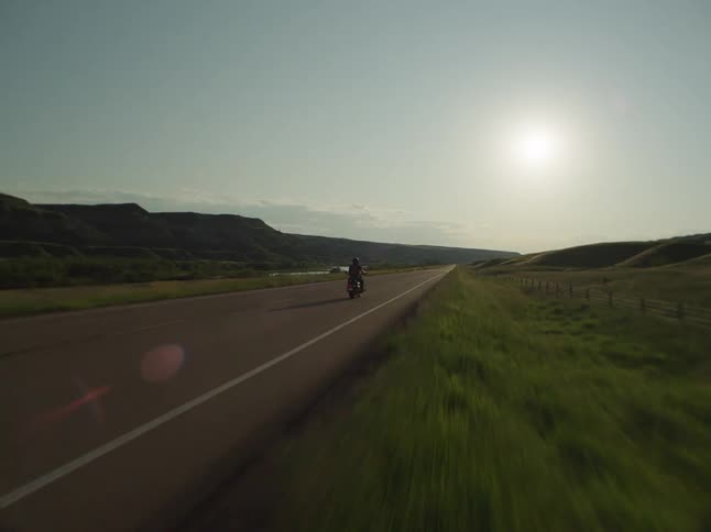 The person is riding the motorcycle down the long road