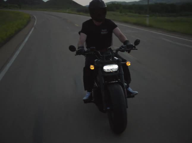 Motorcyclist wearing a helmet rides along a curving road at sunset