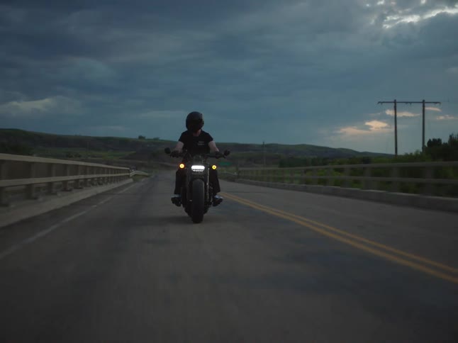Motorcyclist rides along a road under a cloudy sky at dusk