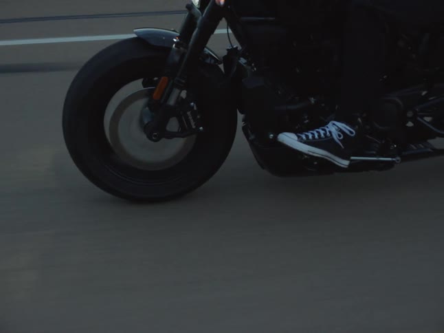 Motorcyclist rides along a road at dusk surrounded by green hills