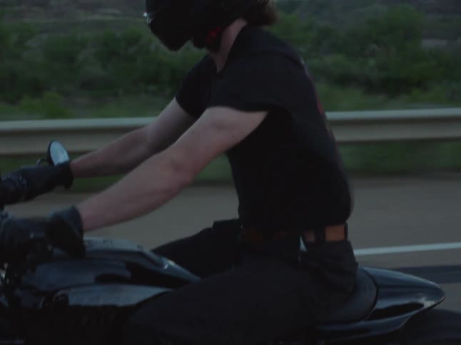 Closeup of a riders white hightop sneaker on the footpeg of a black motorcycle in motion