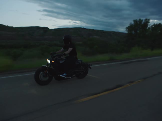 A person riding a motorcycle on a rural road next to a river while wearing a t shirt