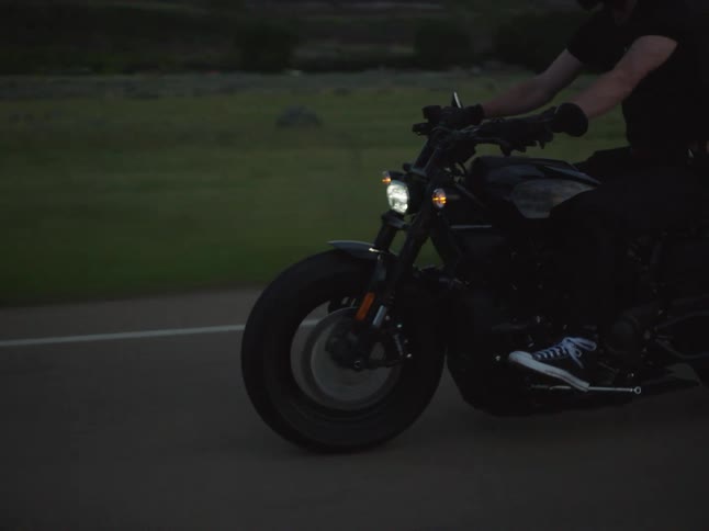 A person rides a motorcycle down an empty rural road at dusk