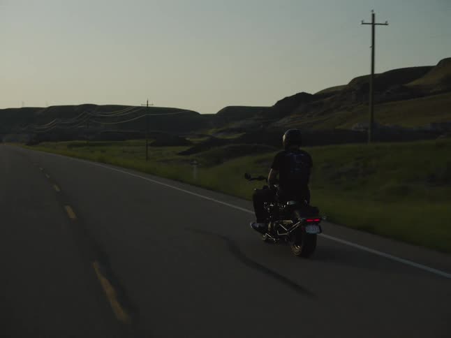 Motorcyclist rides along a road at dusk surrounded by hills