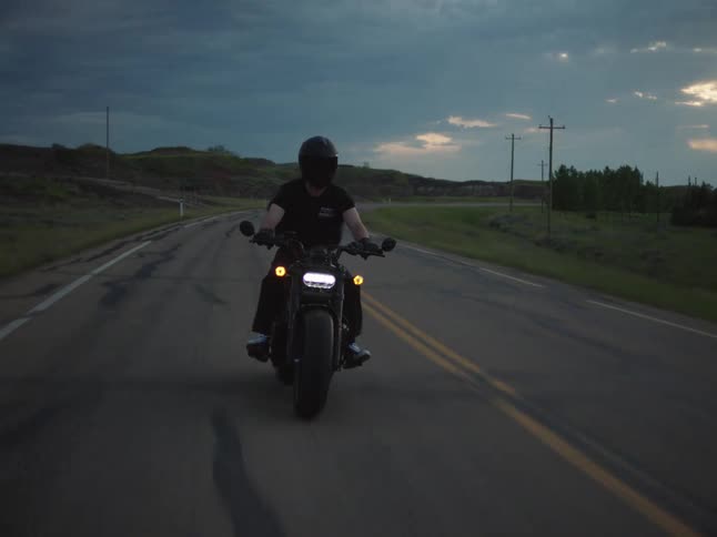 Motorcyclist rides along the road under a dramatic sky at dusk