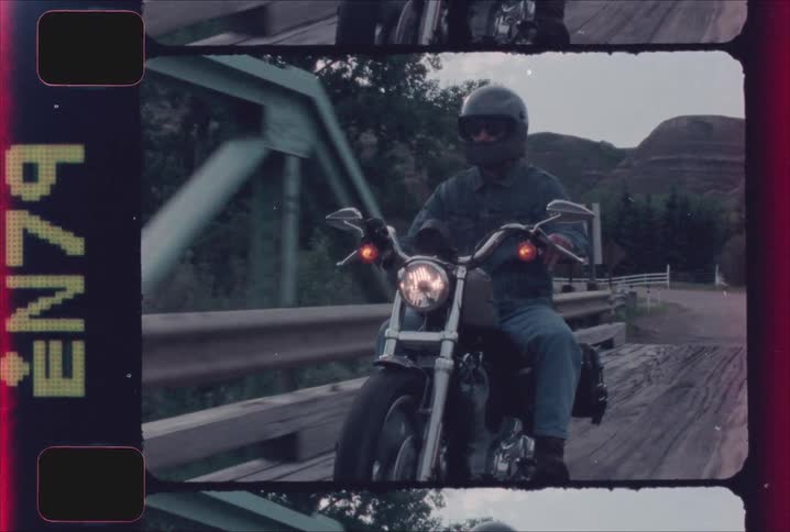 A person in a grey helmet and denim riding a harley davidson motorcycle over a metal bridge