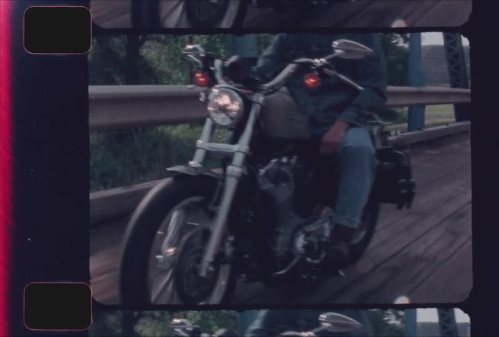 Motorcyclist crosses a narrow bridge wearing a dark jacket and helmet