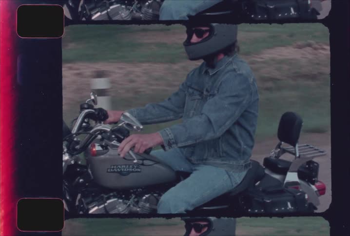 A man in a grey helmet and denim jacket riding a harley davidson motorcycle