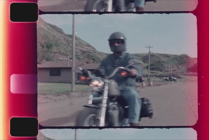 A person in a grey helmet and denim riding a harley davidson motorcycle on a country road with rolling hills in the background