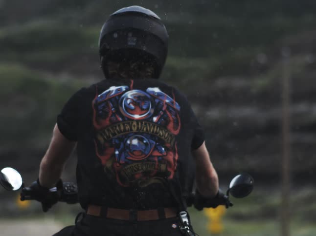 A helmeted motorcyclist in a harleydavidson graphic tee rides through light rain