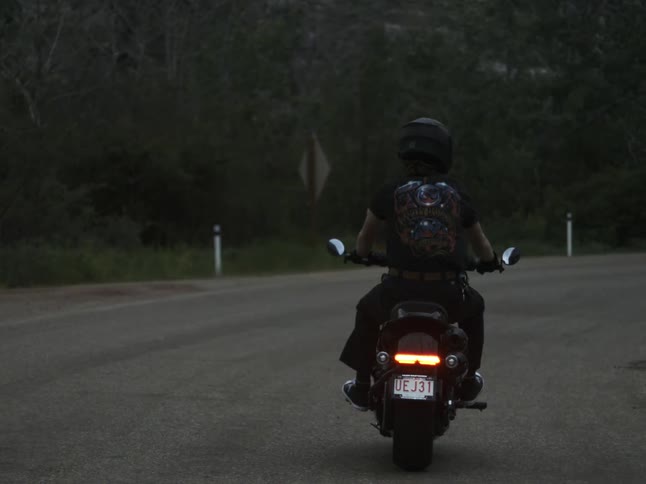 A person rides a motorcycle on the highway at midday wearing a black crash helmet and carrying a backpack