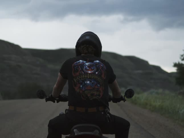 Motorcyclist riding on a road surrounded by hills under a cloudy sky