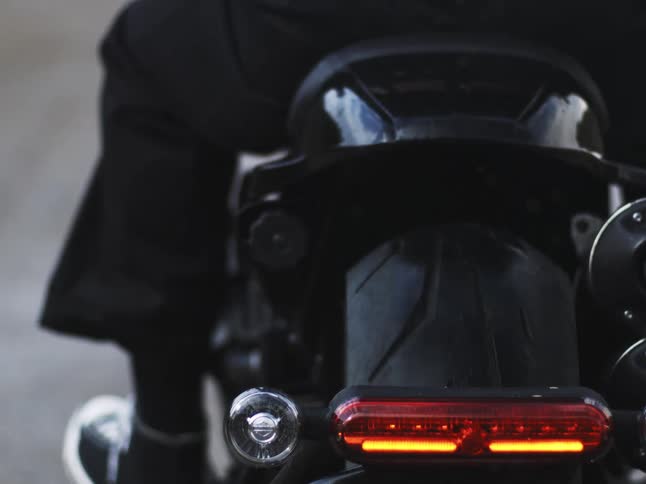 A motorcycles rear shows a bikers leg the back tire and the illuminated tail light with a calgary harley davidson license plate becoming visible