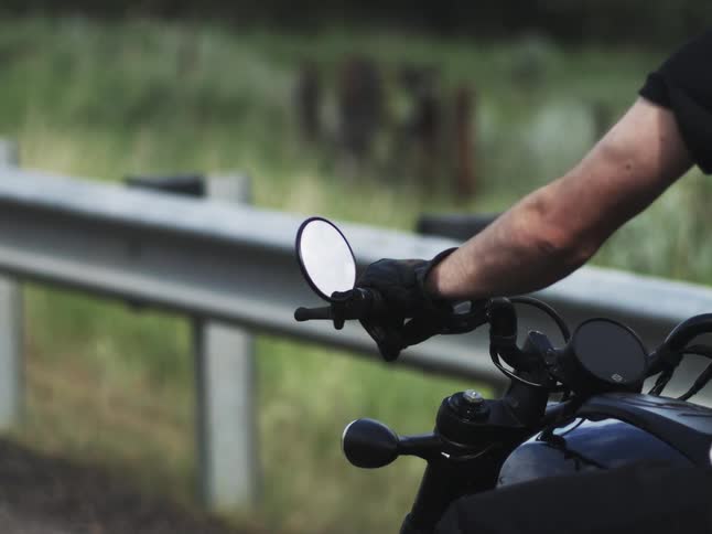 Gloved arm holds the handlebar of a motorcycle near the guardrail