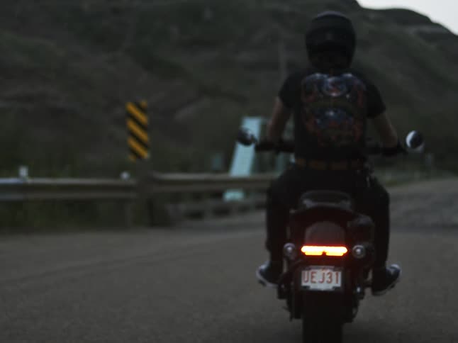 Motorcyclist with rear light on waits stopped on a rural road at dusk