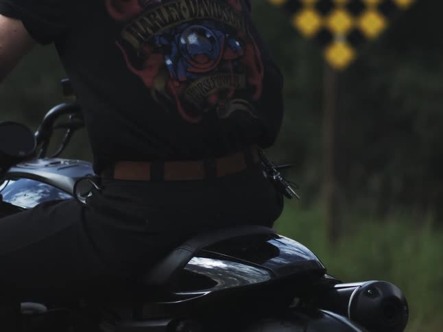 A man in a tshirt riding a motorcycle in the country passing a yellow and black checkered road sign