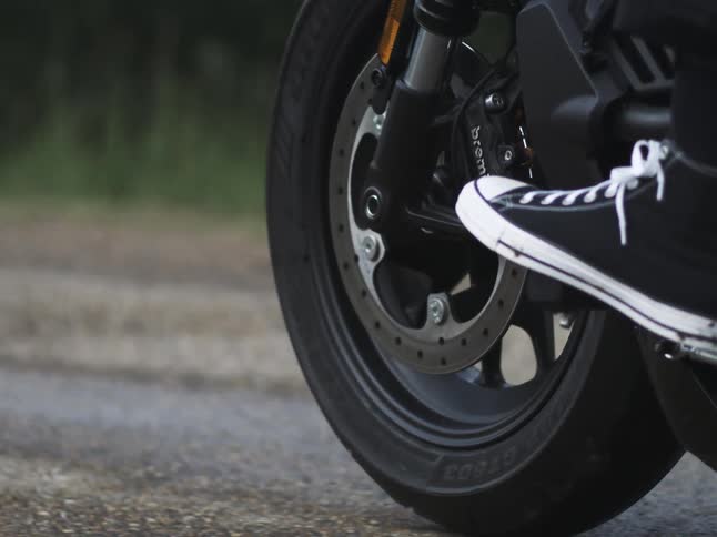 Front motorcycle wheel in focus with a sneaker on the footpeg