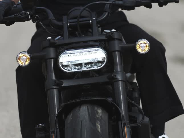 A close view shows the front wheel handlebars and led headlight of a black motorcycle being ridden by a person wearing dark clothes and gloves