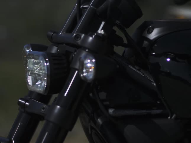 A close view focuses on the front led headlight and black body of a motorcycle with a blurred natural background in the daylight
