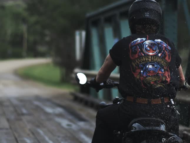 Motorcyclist crosses a wooden bridge wearing a helmet and a black tshirt