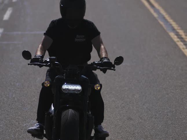 A biker in a dark helmet t shirt and gloves sits on a motorcycle on an asphalt road with its headlights and turn signals illuminated