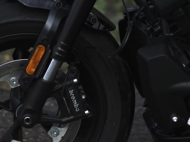 A motorcycles front wheel and engine as it rides on a gravel road