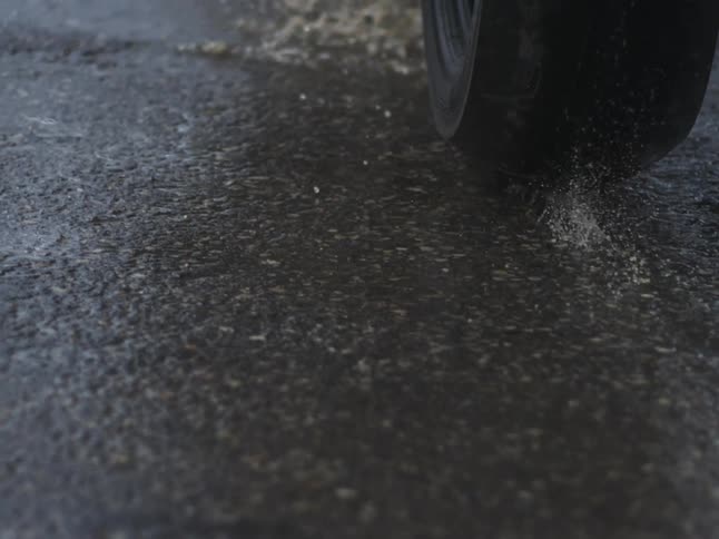 Lowangle closeup of a vehicle tire rolling over rainspeckled asphalt water beading and the road surface glistening