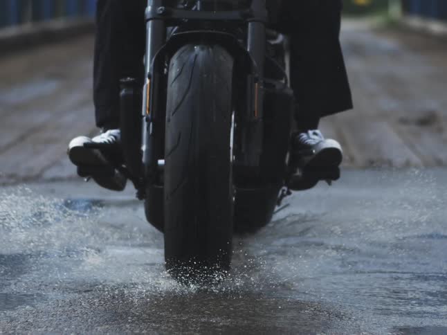 Motorcycles front wheel splashes water droplets while riding over wet ground