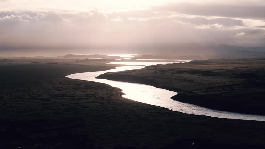 Water stream dividing plain areas of land outdoors during dusk or dawn