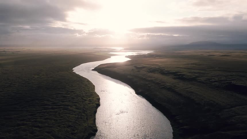 Winding river reflects sunlight as it flows through a vast open landscape