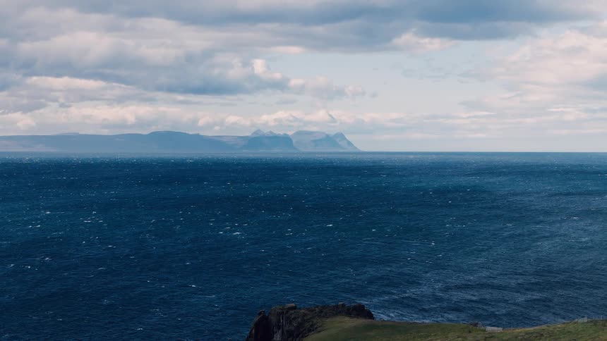 Deep blue sea with mountains in the distance under a partly cloudy sky