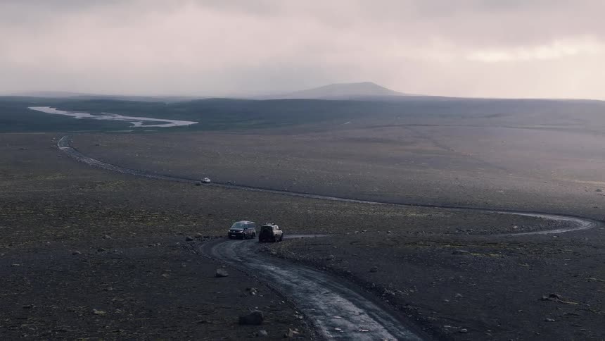 Vehicles pass each other on a highway winding through the wilderness on a foggy overcast day