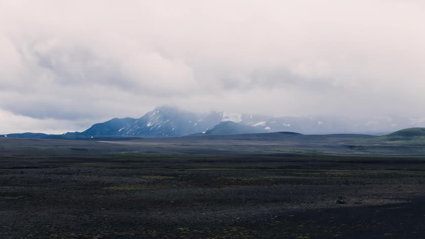 Dark volcanic field stretches toward cloudcovered mountains on the horizon